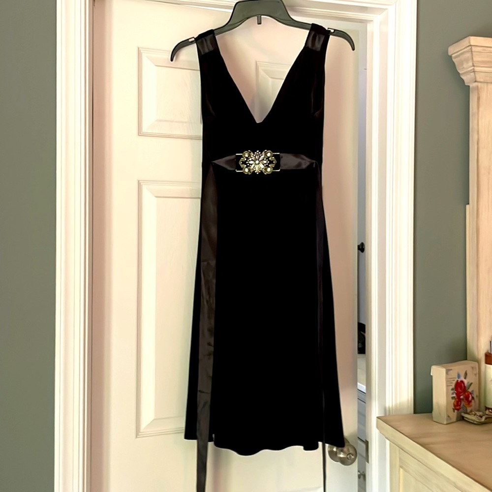 Black dress with silk ties at waist and jeweled pendant on front.